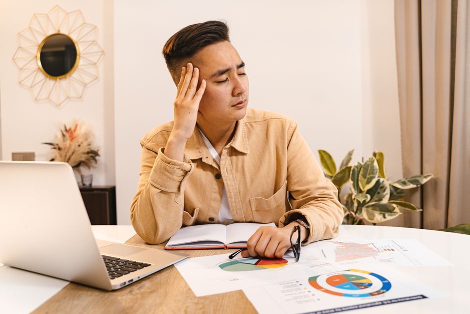 Frustrated man working through paper reports and a laptop at home